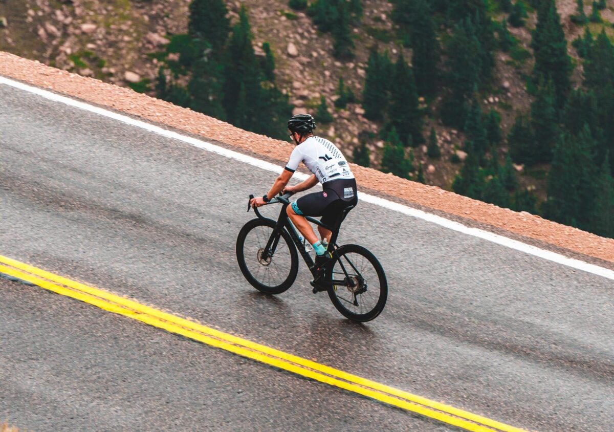 man riding a bicycle on a road near pine tree